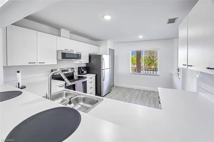 Kitchen with white cabinets, stainless steel appliances, light hardwood / wood-style floors, and sink