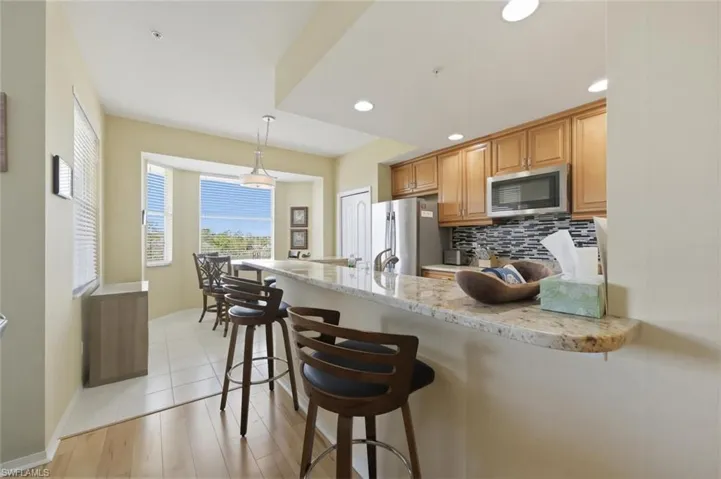 Kitchen with a kitchen bar, decorative backsplash, light stone counters, a peninsula, and stainless steel appliances
