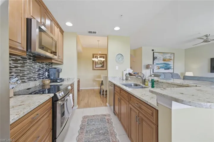 Kitchen with stainless steel appliances, light stone countertops, wood finish cabinetry, open floor plan, and light tile patterned floors