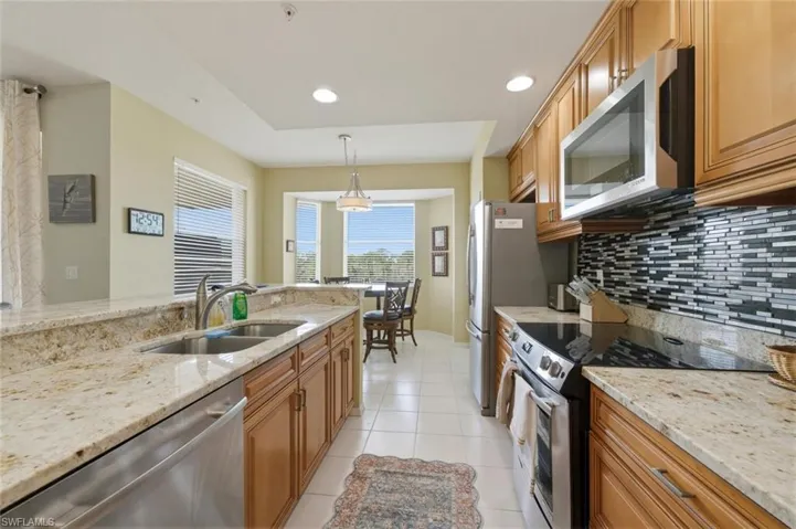 Kitchen with stainless steel appliances, light stone countertops, wood finish cabinets, and hanging light fixtures