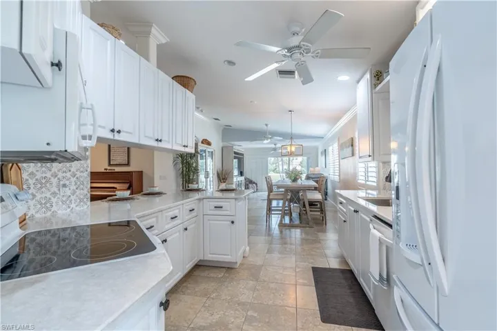 Kitchen with white appliances, kitchen peninsula, ceiling fan, hanging light fixtures, and white cabinets