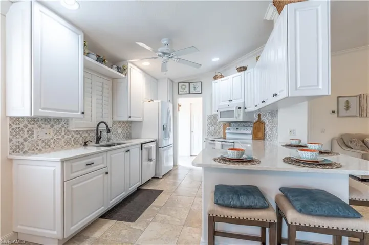 Kitchen with white appliances, a kitchen bar, kitchen peninsula, sink, and ceiling fan