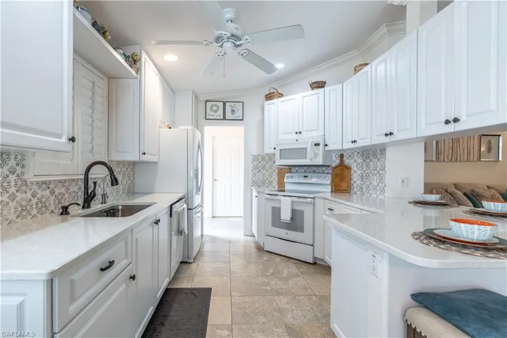 Kitchen with white cabinetry, white appliances, sink, and ceiling fan