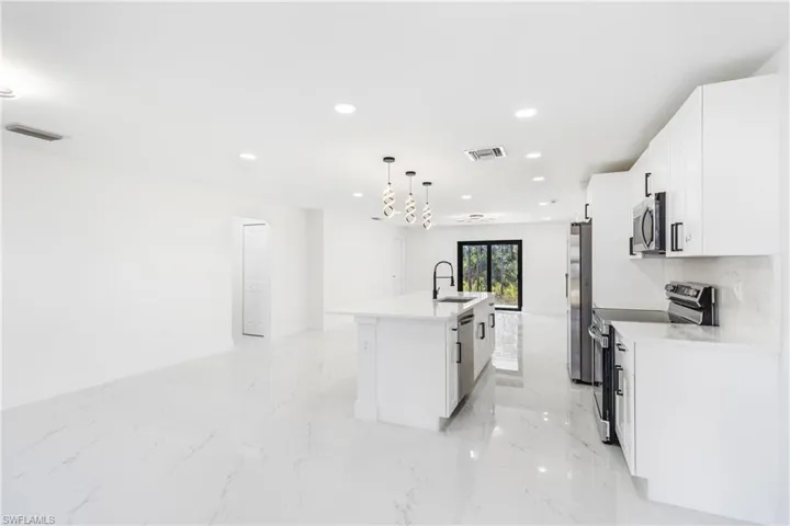 Kitchen with stainless steel appliances, an island with sink, white cabinets, decorative light fixtures, and recessed lighting