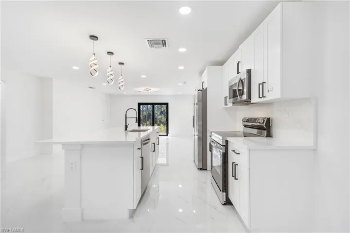 Kitchen with stainless steel appliances, light marble finish flooring, a kitchen island with sink, pendant lighting, and white cabinets