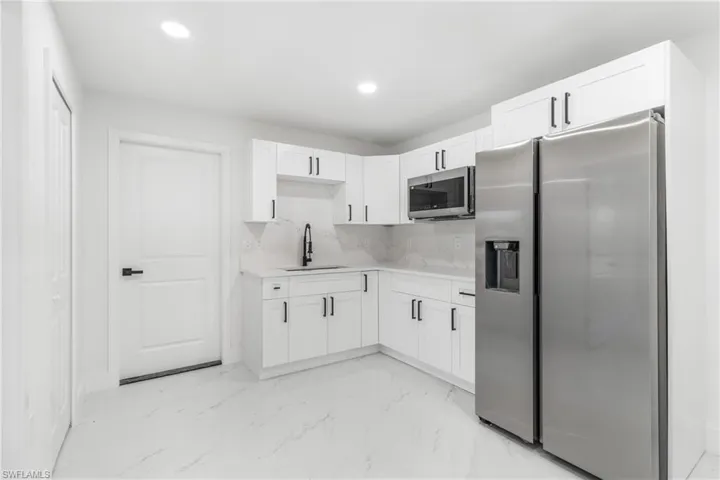 Kitchen featuring appliances with stainless steel finishes, tasteful backsplash, white cabinets, light marble finish floors, and recessed lighting