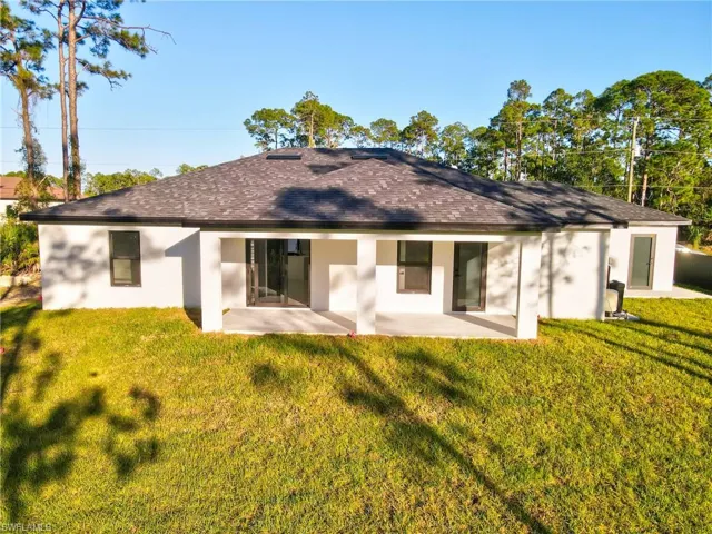 Rear view of house featuring stucco siding, a yard, roof with shingles, and a patio