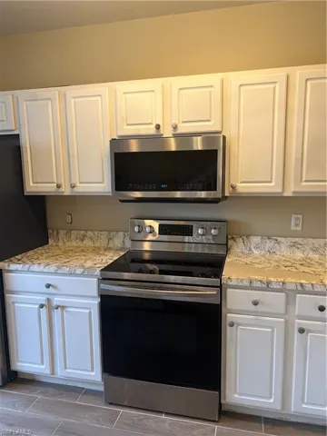 Kitchen featuring white cabinetry, stainless steel range, refrigerator, and light stone counters