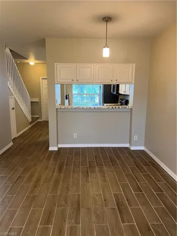 Kitchen featuring light stone countertops, kitchen peninsula, dark wood-type flooring, decorative light fixtures, and white cabinetry