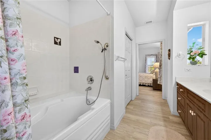 Full bath featuring shower / bath combination with curtain, vanity, ensuite bath, and light wood-style floors