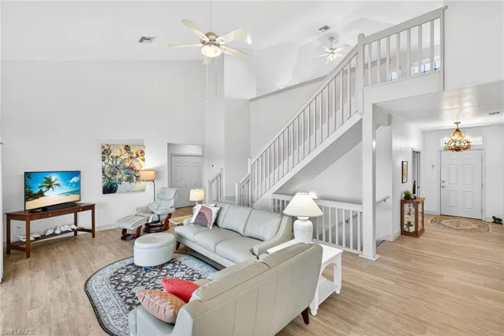 Living area featuring high vaulted ceiling, light wood-style flooring, and stairway