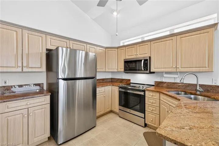 Kitchen with stainless steel appliances, dark stone counters, high vaulted ceiling, light tile patterned floors, and ceiling fan