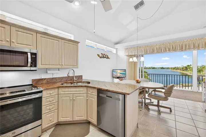 Kitchen with appliances with stainless steel finishes, light stone counters, lofted ceiling, light tile patterned floors, and a peninsula