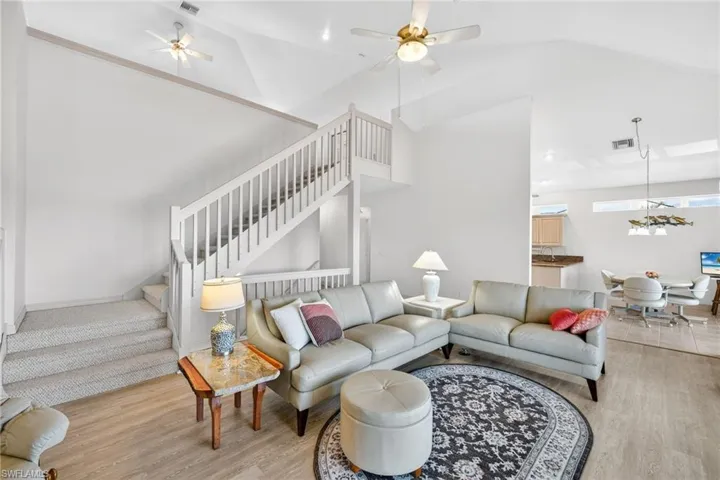 Living room featuring stairway, light wood finished floors, ceiling fan, and high vaulted ceiling