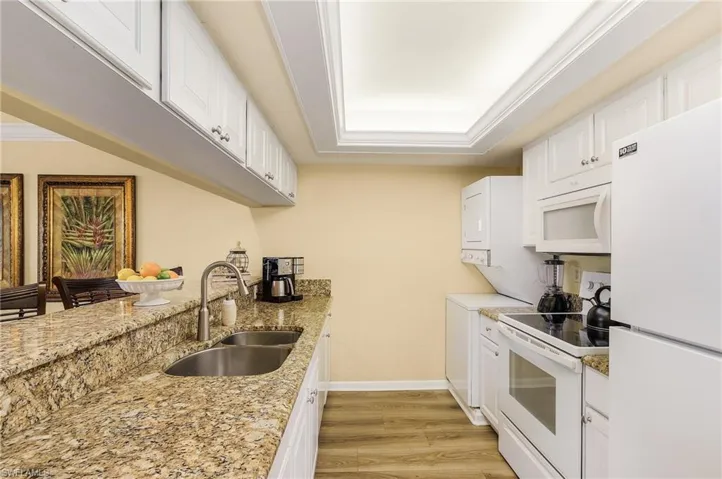 Kitchen featuring stacked washer and clothes dryer, white appliances, a tray ceiling, sink, and light hardwood / wood-style floors