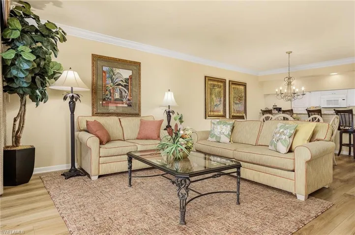 Living room with crown molding, a notable chandelier, and light wood-type flooring