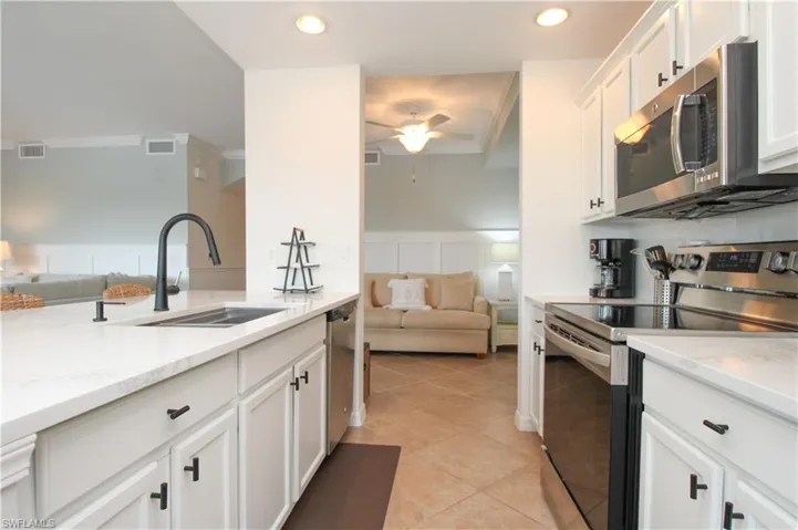Kitchen with sink, light stone countertops, light tile patterned floors, appliances with stainless steel finishes, and white cabinetry