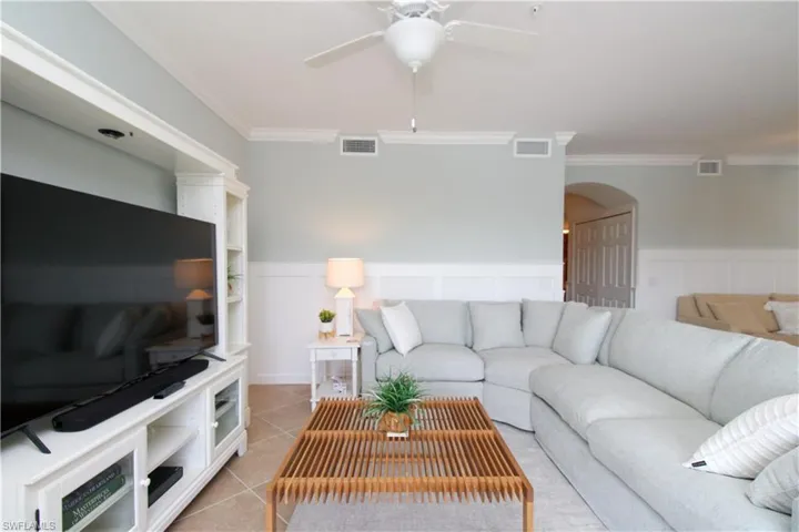 Living room with ceiling fan, light tile patterned floors, and ornamental molding