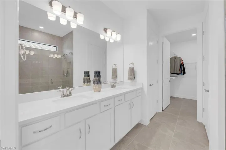 Bathroom featuring double vanity, a stall shower, light tile patterned flooring, a spacious closet, and recessed lighting
