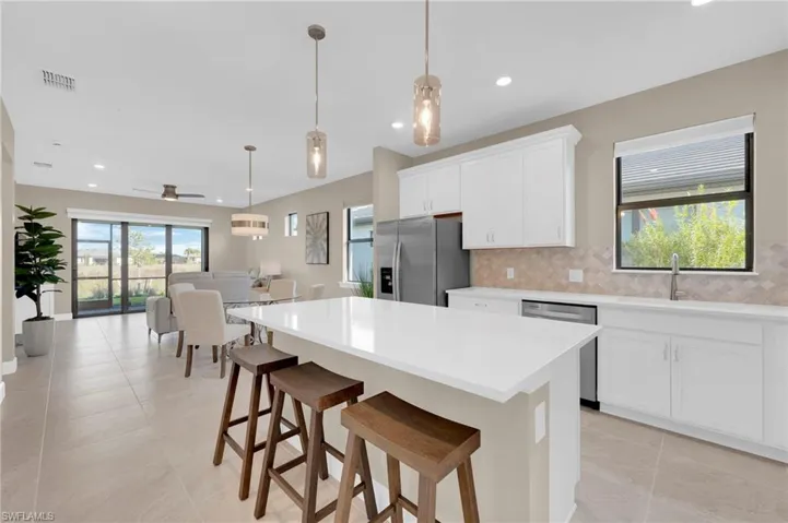 Kitchen with white cabinetry, a kitchen bar, hanging light fixtures, appliances with stainless steel finishes, and a kitchen island