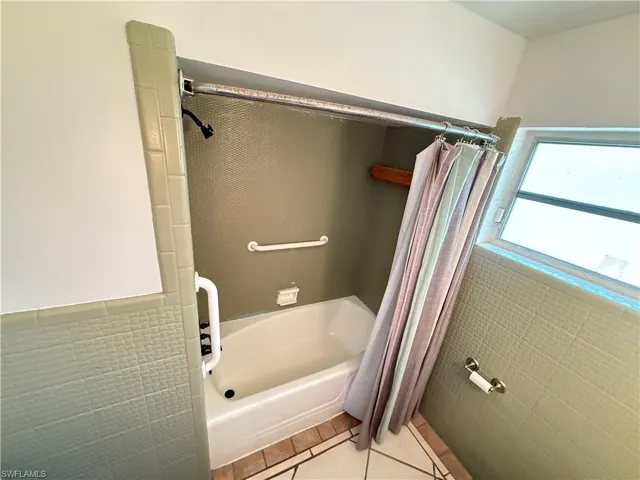 Bathroom featuring tile walls, light tile patterned floors, wainscoting, and shower / bath combo with shower curtain