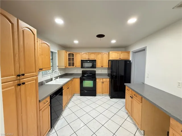 Kitchen with black appliances, glass insert cabinets, dark countertops, recessed lighting, and light tile patterned floors