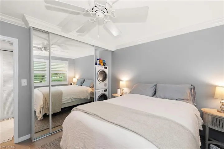 Bedroom featuring crown molding, stacked washer and dryer, a ceiling fan, wood finished floors, and closet