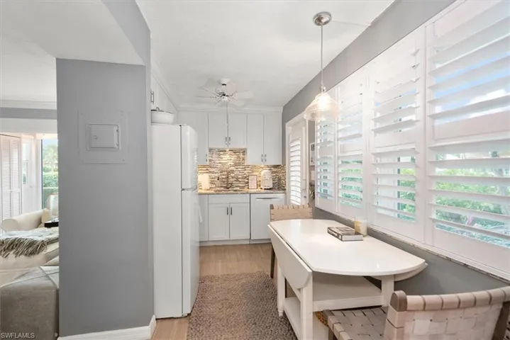 Kitchen featuring white cabinets and appliances, decorative light fixtures, light wood-style floors, and decorative backsplash