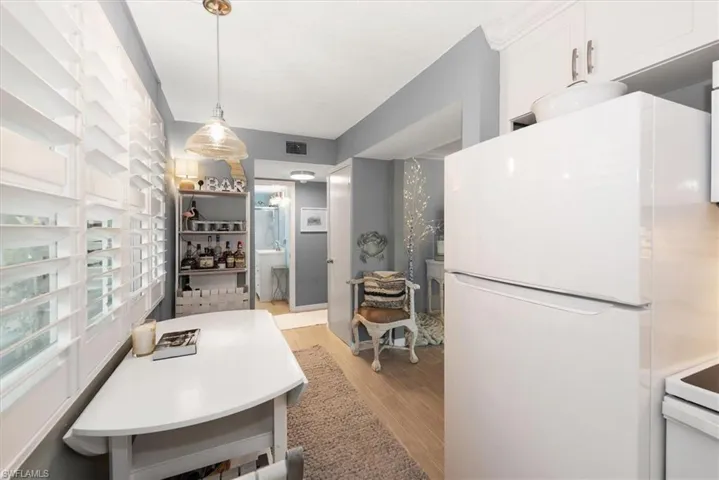 Kitchen with white appliances, light wood finished floors, white cabinets, and hanging light fixtures