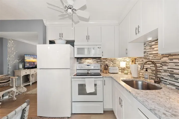 Kitchen with white appliances, white cabinetry, crown molding, light stone counters, and backsplash