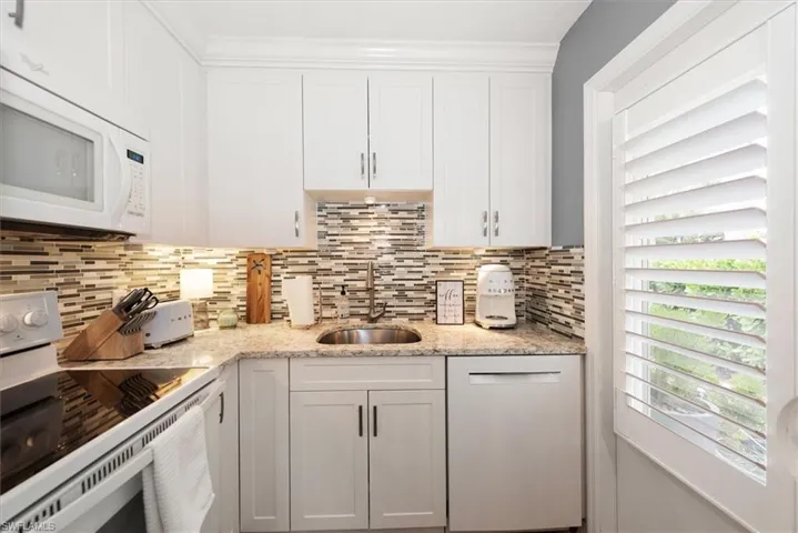 Kitchen with white appliances, white cabinets, light stone countertops, and tasteful backsplash