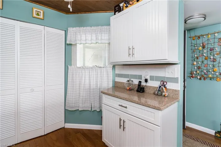 Kitchen with light stone countertops, white cabinets, wood flooring and ceiling, and tasteful backsplash