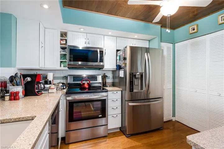 Kitchen with white cabinets, tasteful backsplash, light wood flooring, and appliances with stainless steel finishes
