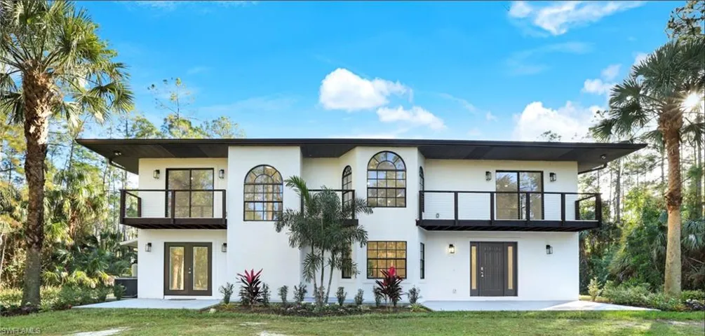 Front of house featuring a lawn, a balcony, and french doors