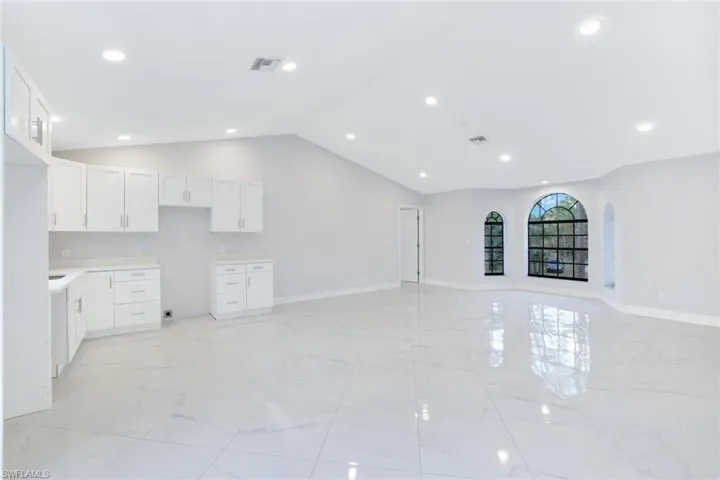 2nd floor kitchen with white cabinets, vaulted ceiling, living room area and sliding glass door leading to the balcony