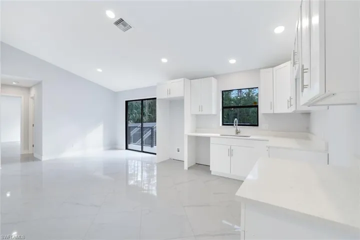 2nd floor kitchen with vaulted ceiling, white cabinetry, and sliding glass doors leading to the balcony