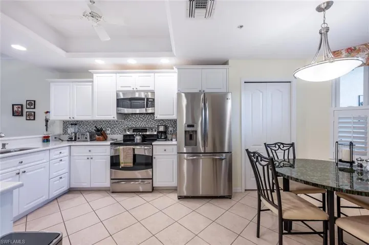 Kitchen with a raised ceiling, appliances with stainless steel finishes, and white cabinetry