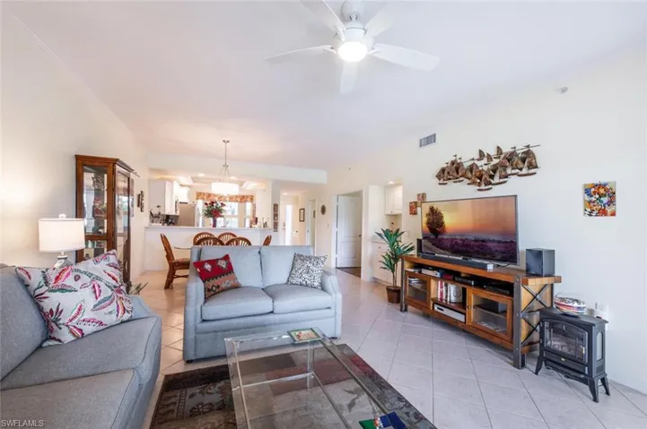 Living room with a wood stove, light tile patterned floors, ceiling fan, and crown molding