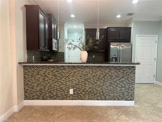 Kitchen with stainless steel appliances, tasteful backsplash, crown molding, pendant lighting, and dark stone countertops
