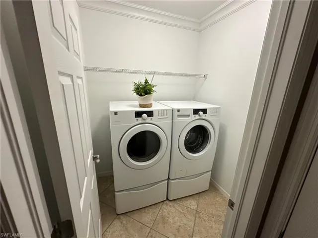 Washroom featuring crown molding, washer and clothes dryer, and light tile patterned flooring