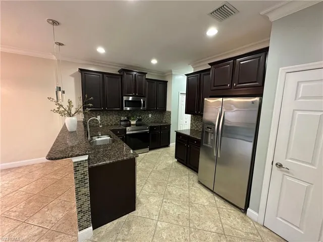 Kitchen with dark stone countertops, ornamental molding, stainless steel appliances, a peninsula, and pendant lighting