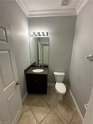 Half bathroom with vanity, crown molding, and light tile patterned flooring