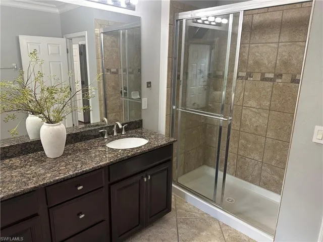 Bathroom featuring a stall shower, vanity, ornamental molding, and light tile patterned flooring