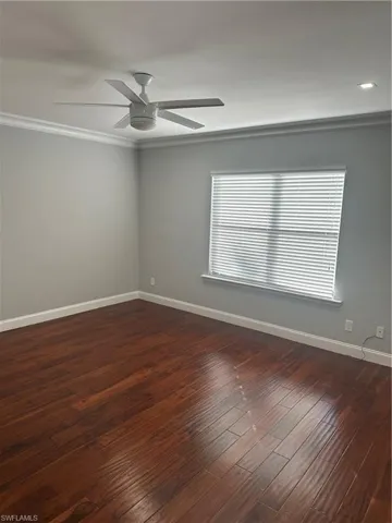Empty room featuring dark wood-style floors, ornamental molding, and ceiling fan