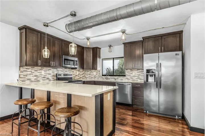 Kitchen with wood finish cabinetry, stainless steel appliances, a peninsula, and dark wood-type flooring