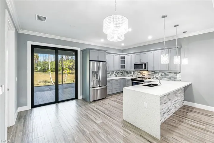 Kitchen featuring gray cabinetry, stainless steel appliances, ornamental molding, light stone countertops, and glass fronted cabinets