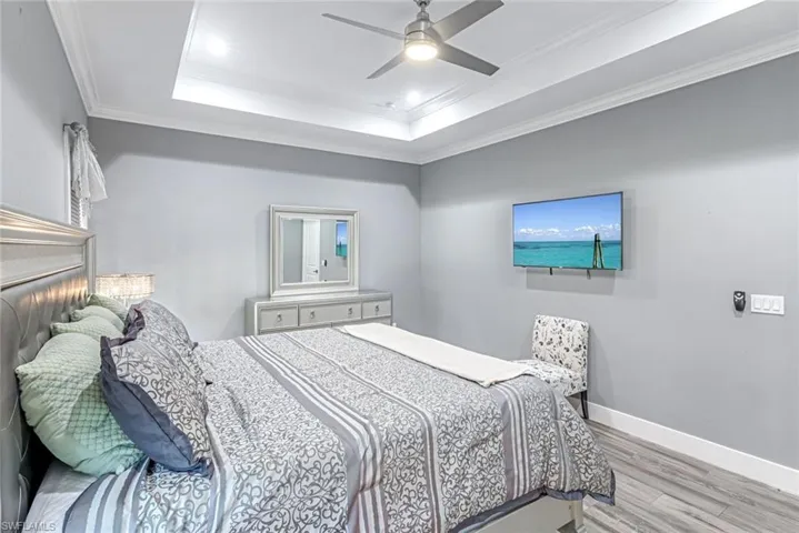 Bedroom with ornamental molding, light wood-type flooring, ceiling fan, and a raised ceiling