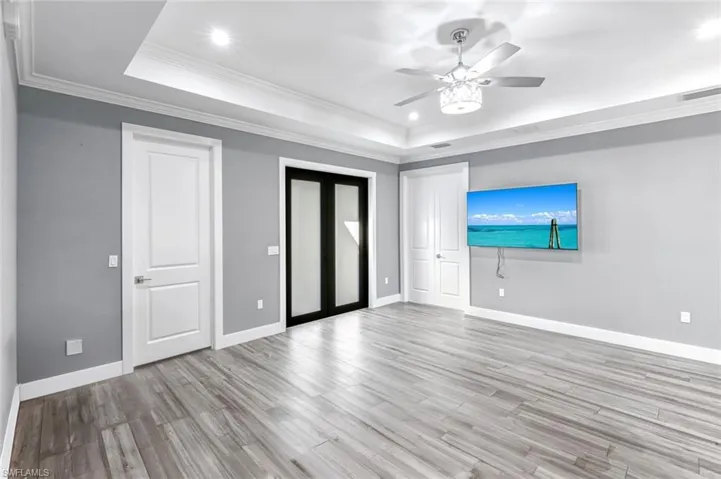 Unfurnished bedroom featuring crown molding, light wood-style flooring, recessed lighting, a ceiling fan, and a raised ceiling