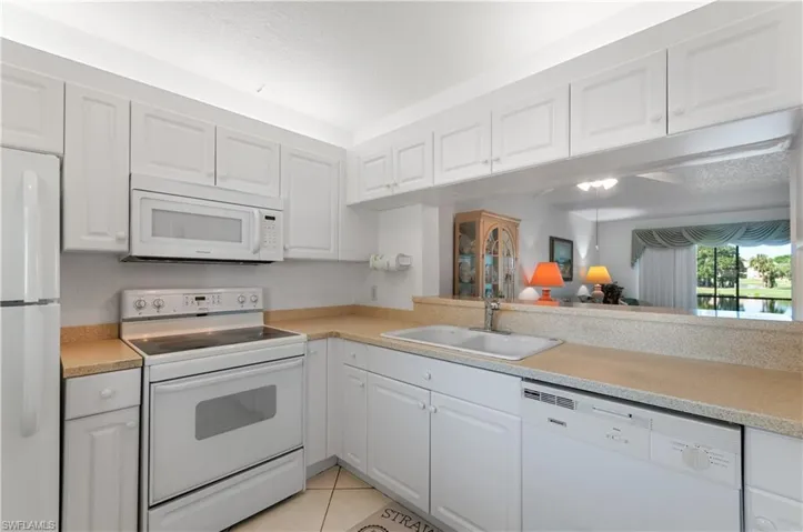 Kitchen featuring sink, white cabinetry, light tile patterned flooring, and white appliances