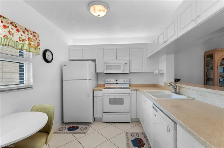 Kitchen featuring light tile patterned floors, sink, white appliances, and white cabinets